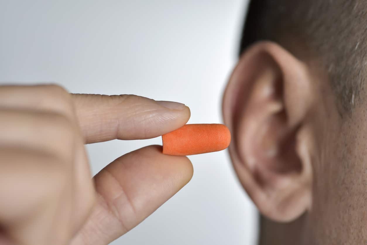 Man inserting an orange foam earplug into his ear for hearing protection