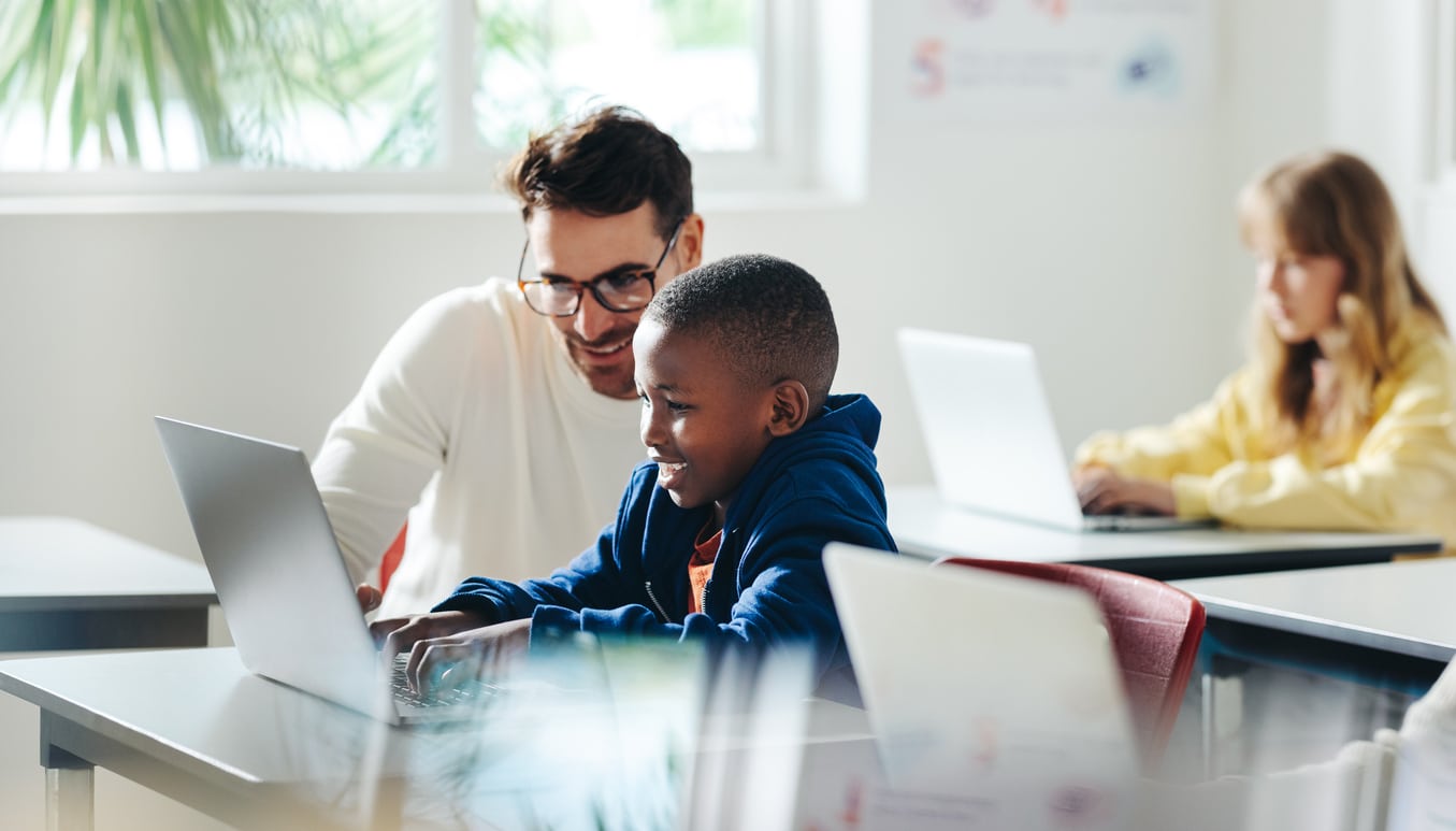 Teacher helping a young boy in computer class.